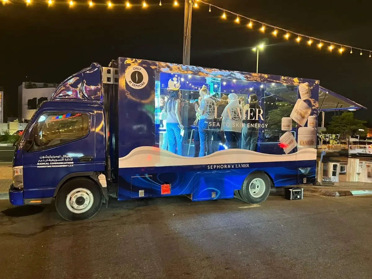 Glass display truck at an evening brand activation in Dubai, lit from inside with guests browsing the product display